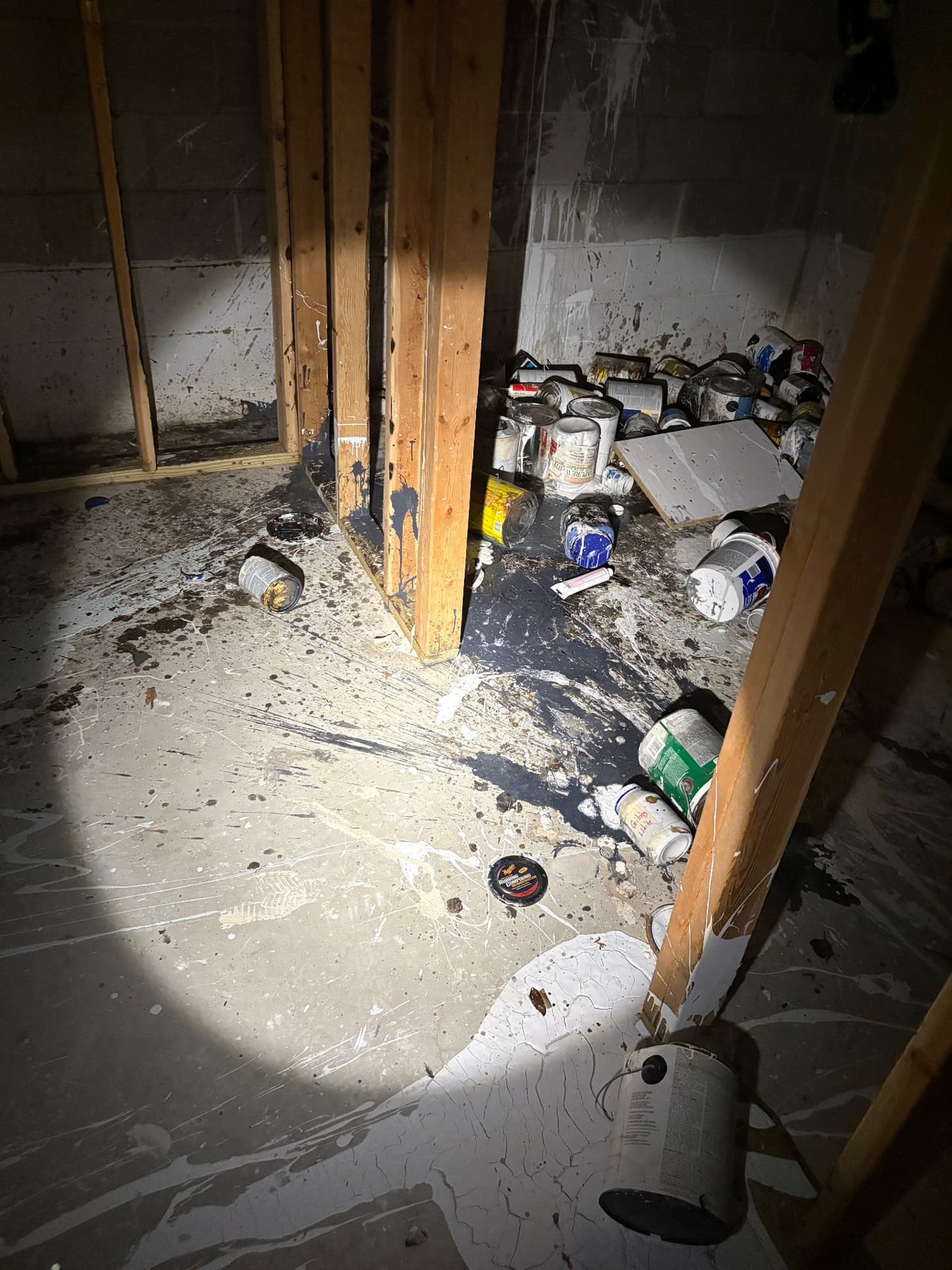 Vacant property basement with spilled paint across the floor and abandoned paint cans stacked against the wall