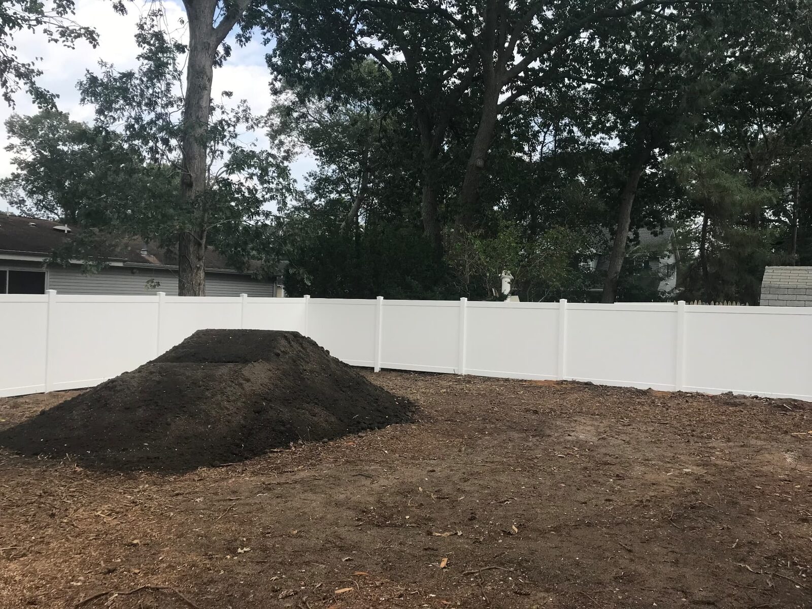 Cleared rear yard with a new white vinyl fence and a delivered pile of topsoil ready for grading