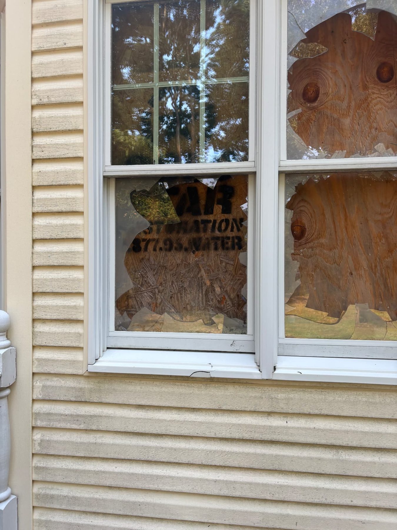 Broken exterior window on a vacant property with plywood board-up installed behind the damaged glass