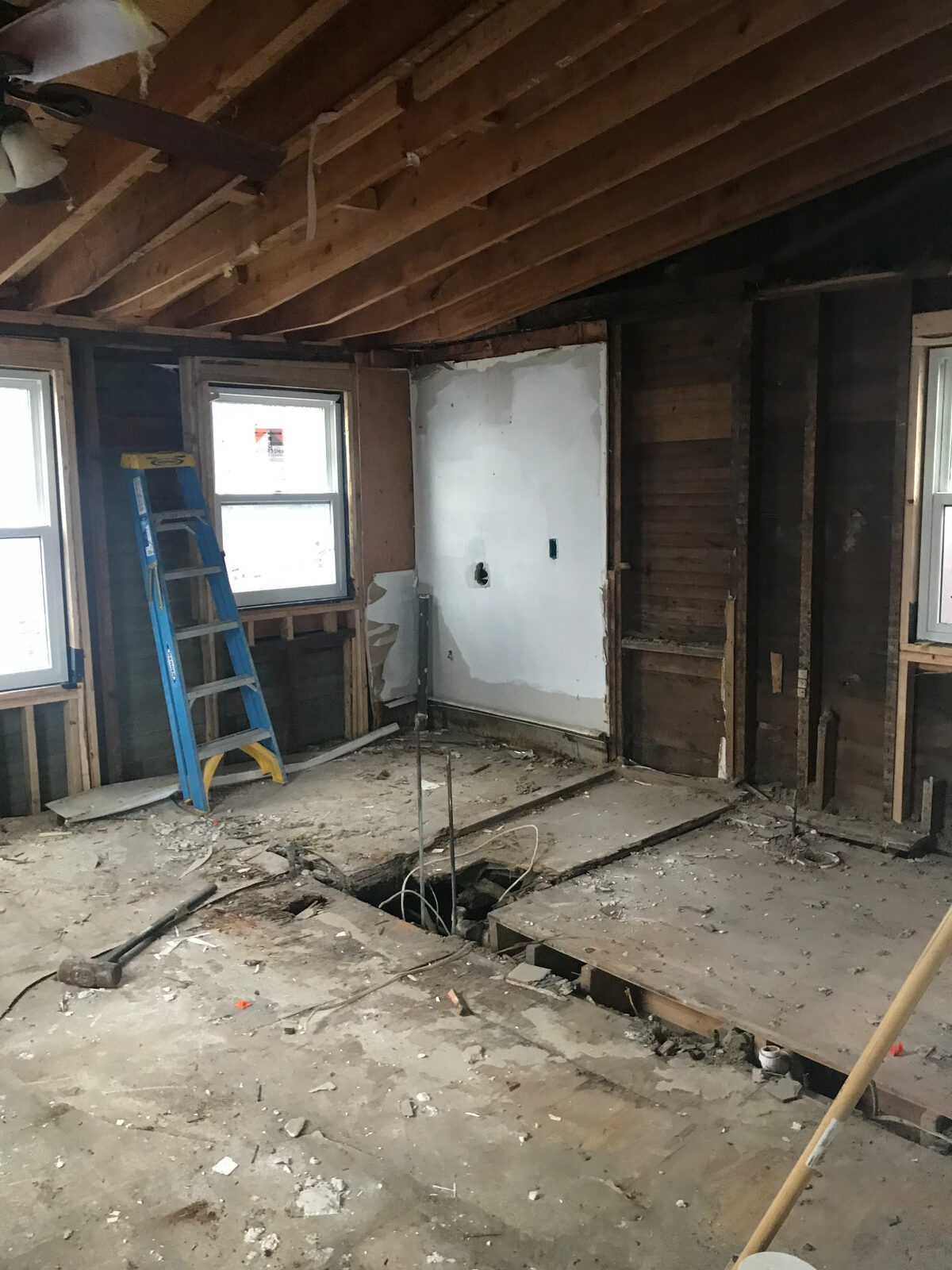 Interior room taken down to studs and joists with a large section of subfloor removed