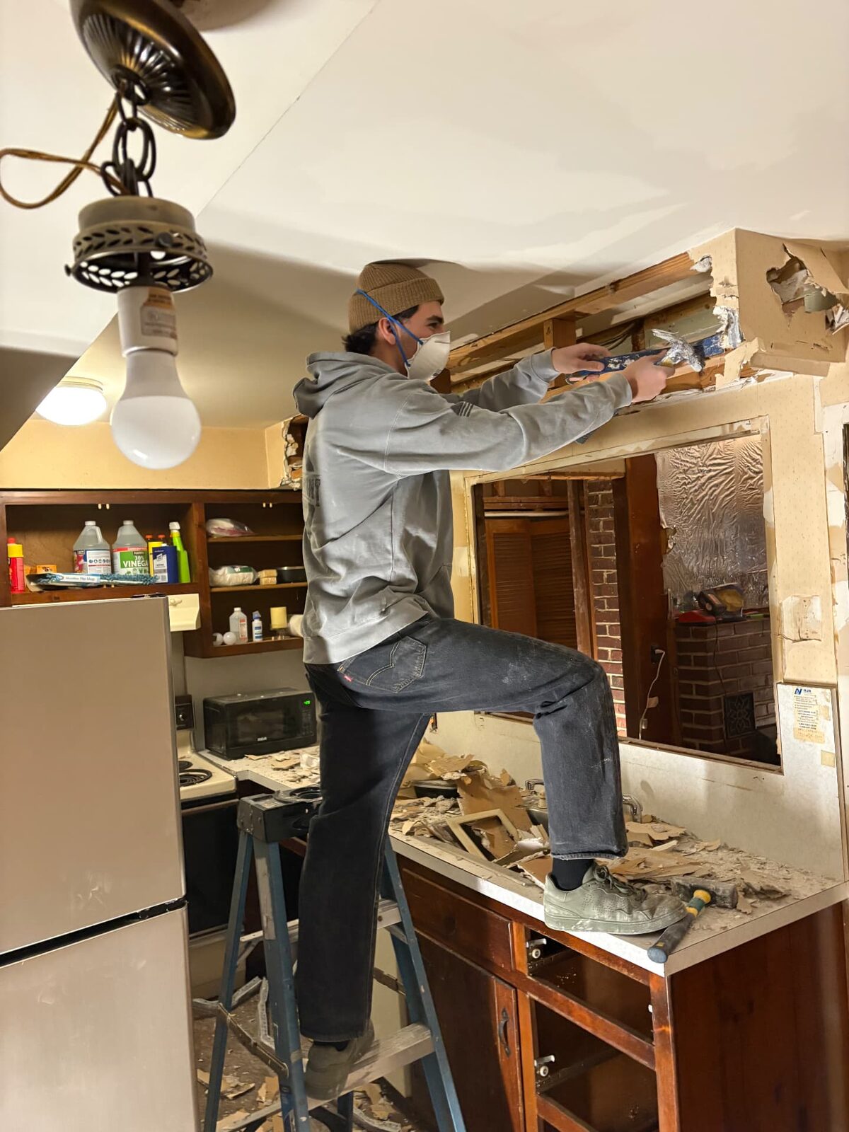 Worker in a dust mask cutting out a kitchen soffit and upper cabinetry during demolition