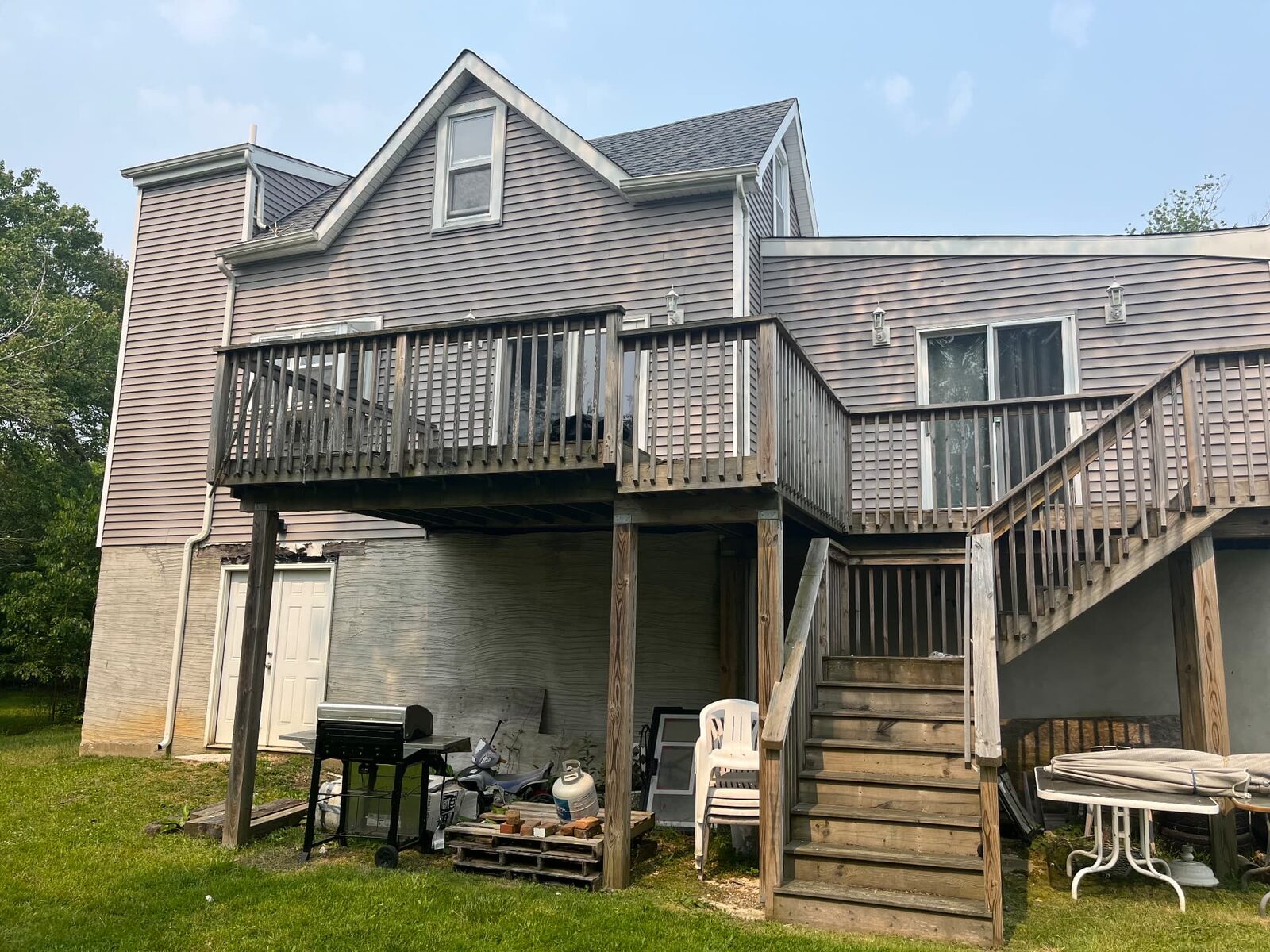 Rear exterior of a property with weathered siding, an aging deck and items stored underneath