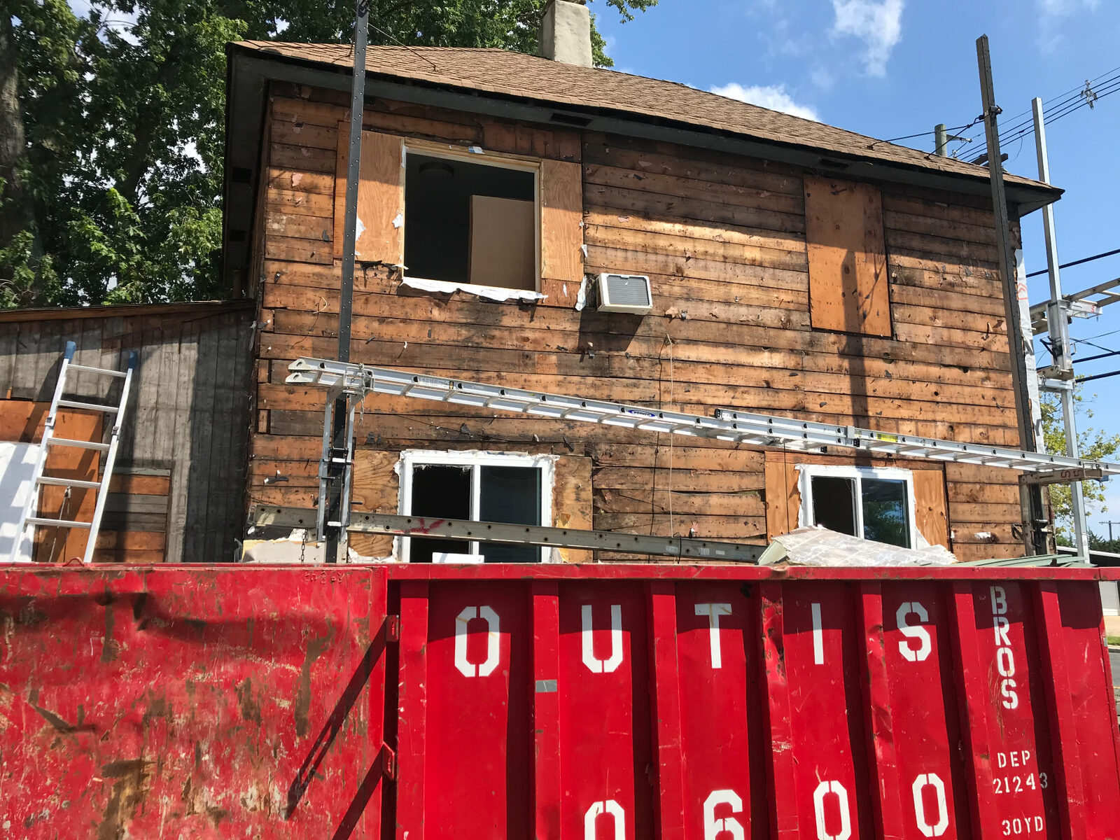 House exterior stripped back to sheathing with a roll-off dumpster staged in front for debris
