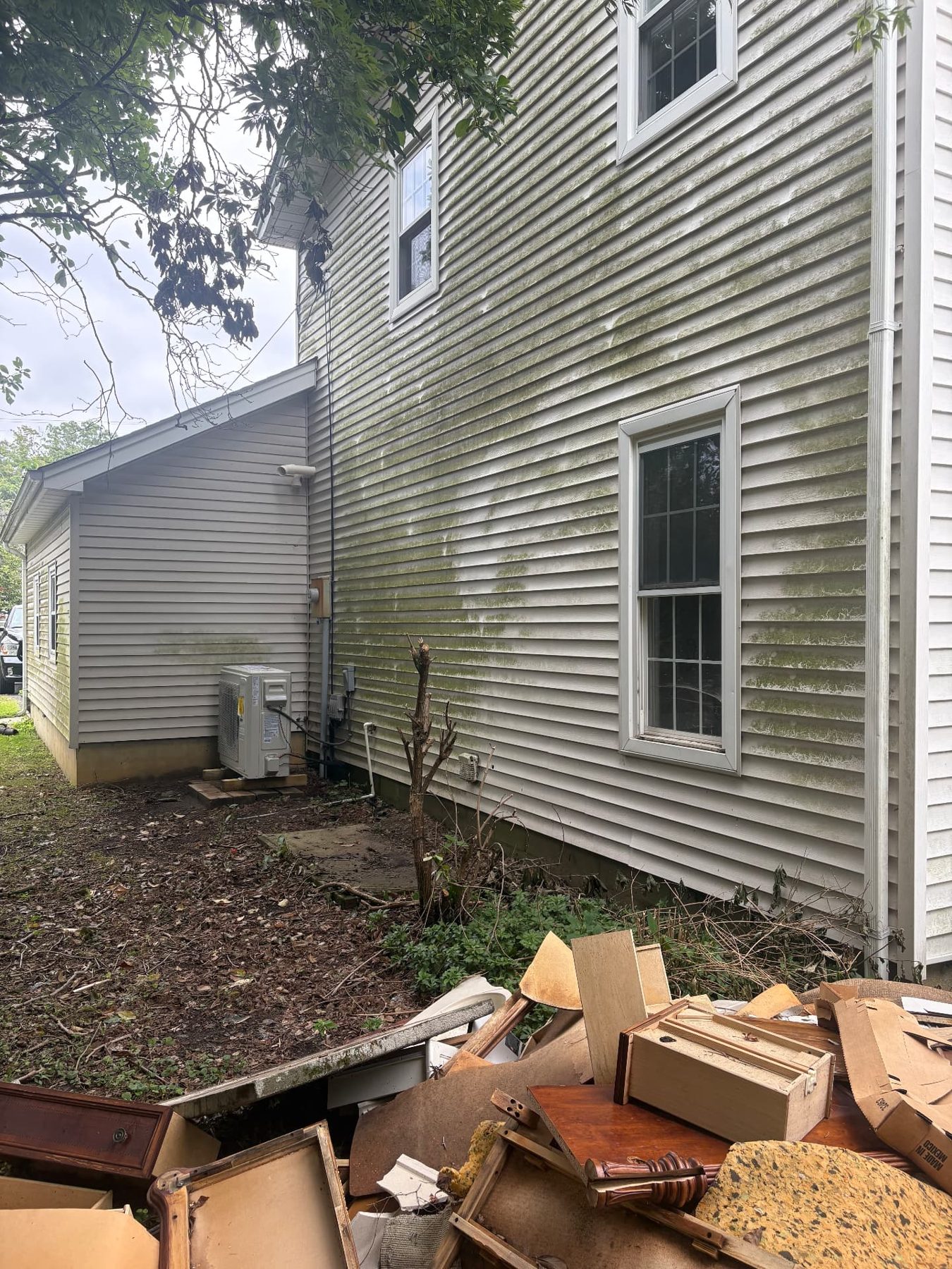 Side elevation of a vacant property with algae-stained siding and removed contents piled outside for disposal