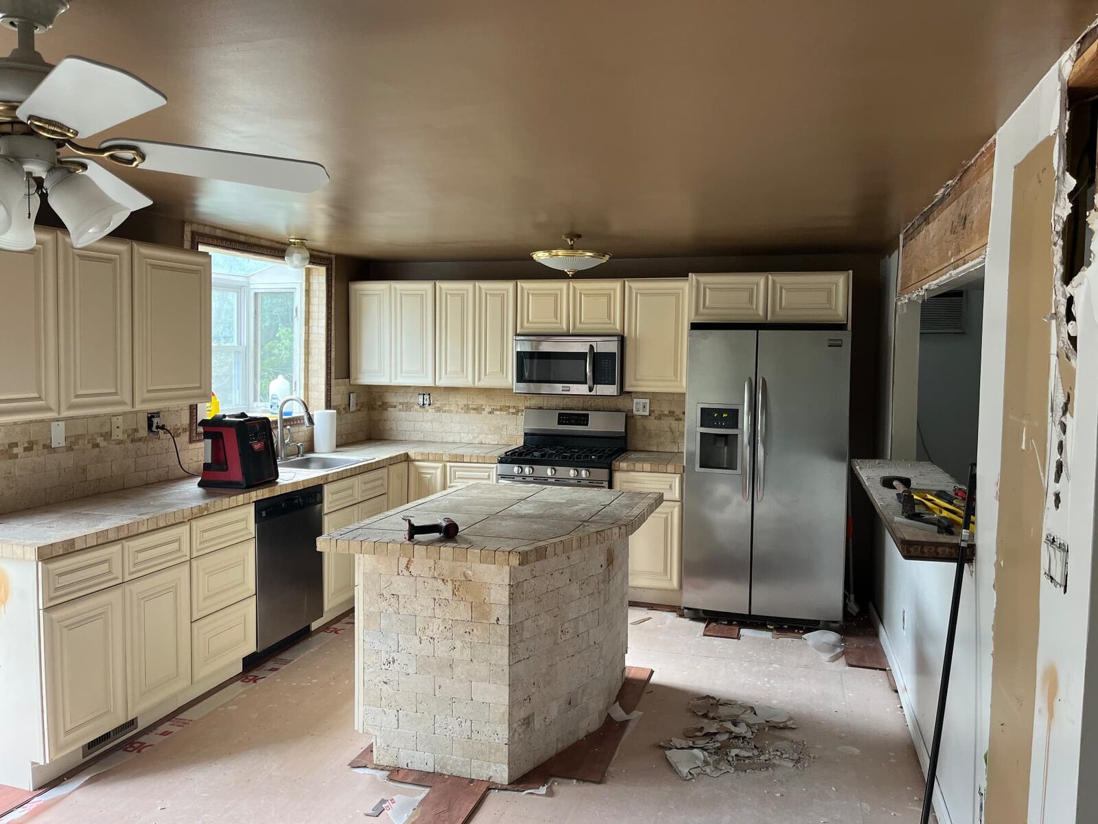Dated kitchen before improvement work, with older cabinetry, tile counters and a tiled island