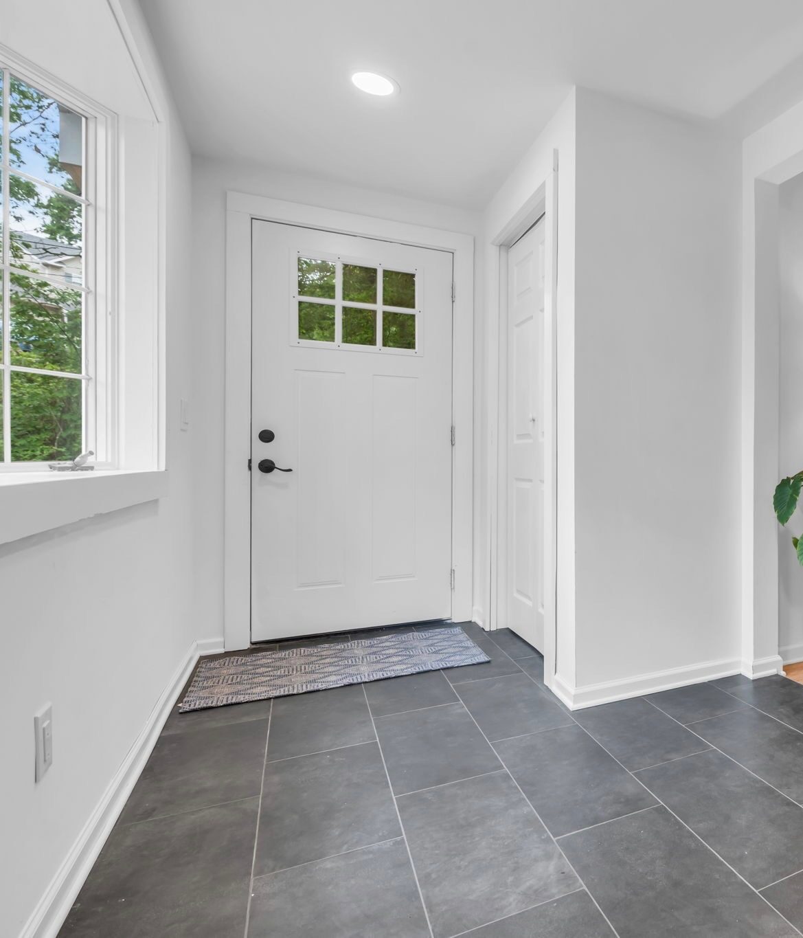 Finished interior entry hall with large-format dark tile flooring, white walls, new door and trim