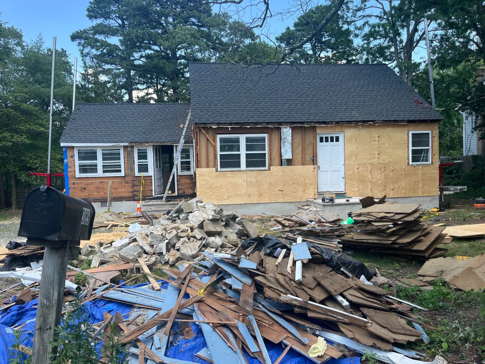 Home exterior with tear-off debris and lumber piled in the front yard on tarps for removal