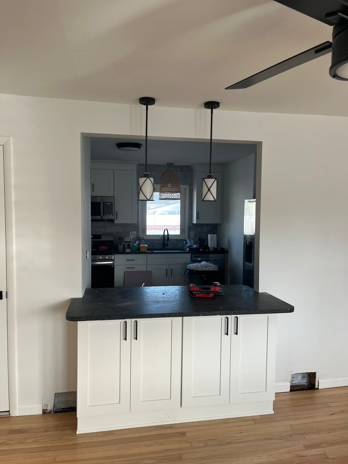 Finished kitchen with white shaker cabinetry, dark countertop peninsula and pendant lighting over a pass-through opening