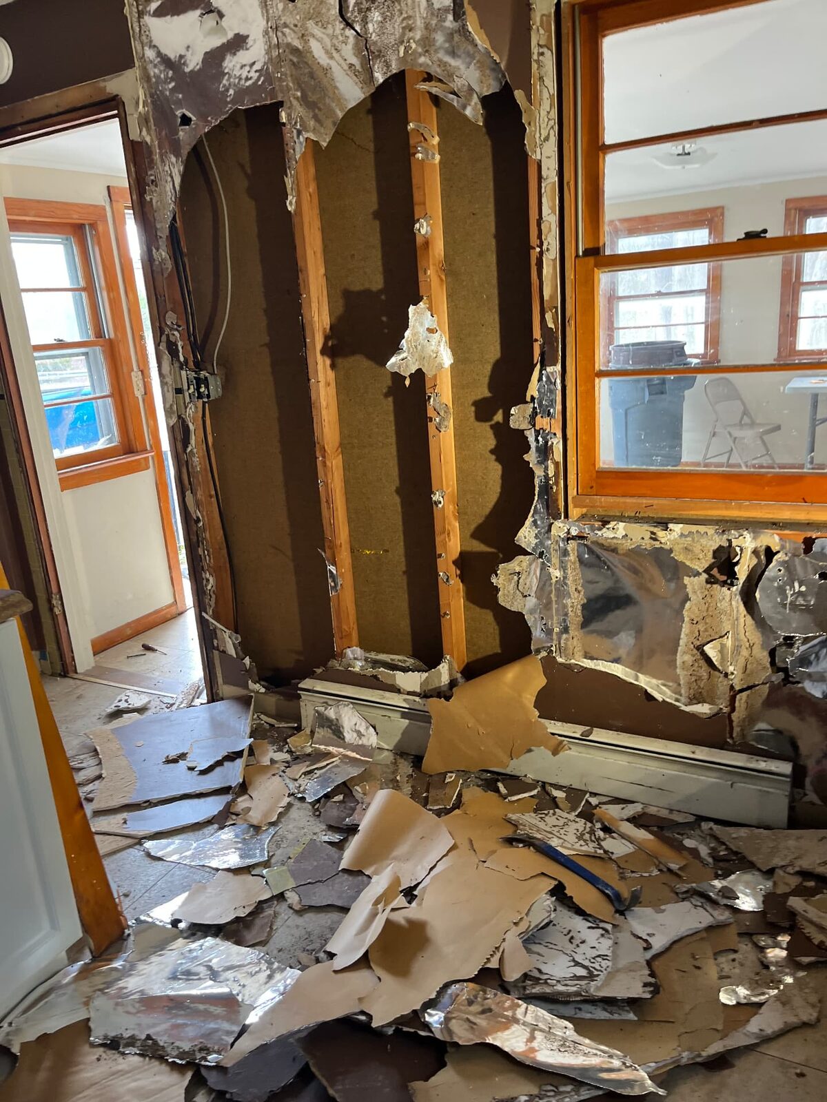 Interior wall opened during demolition exposing studs and insulation, with debris on the floor