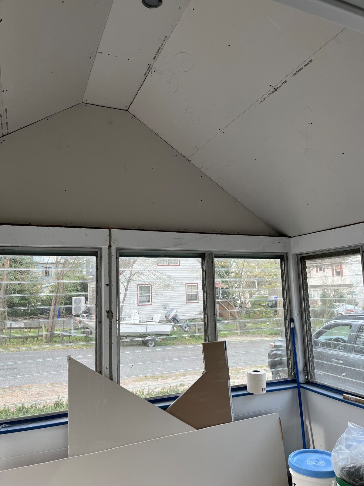 Room with a vaulted ceiling newly drywalled, with a wall of windows and materials still on site
