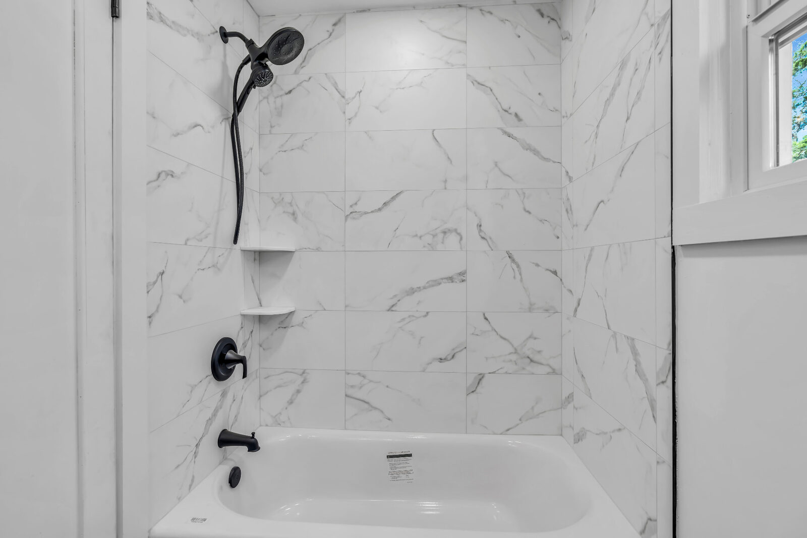 Finished bathroom with a marble-pattern tiled tub surround, new tub and black fixtures