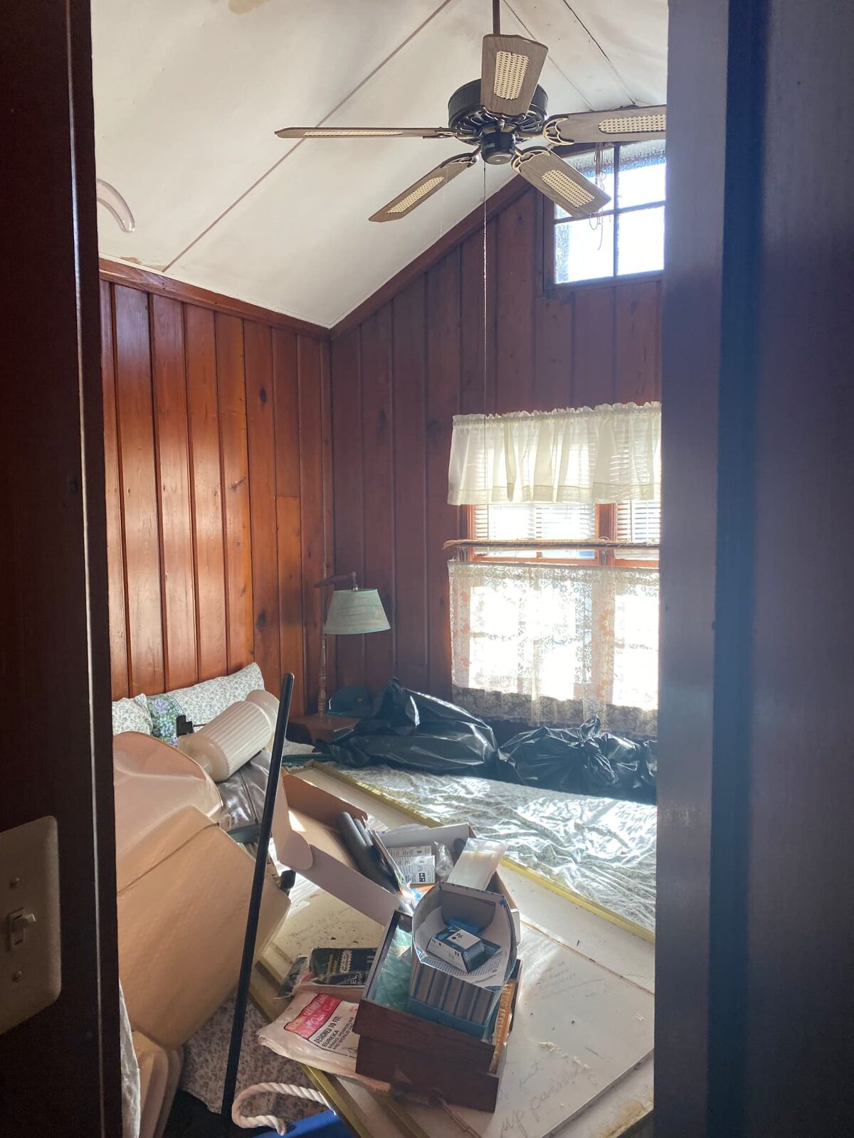 Wood-paneled bedroom filled with furniture, boxes and bagged contents before removal